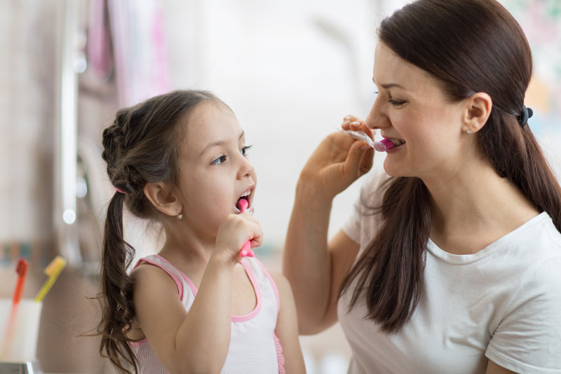 a mother and daughter brushing their teeth together so the daughter does not get gum disease.