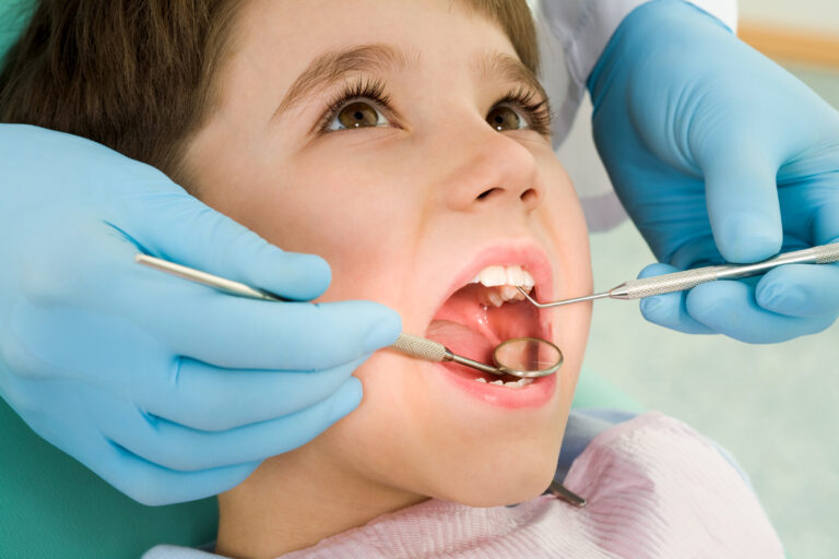 Close-up of little boy opening his mouth wide during inspection of oral cavity.